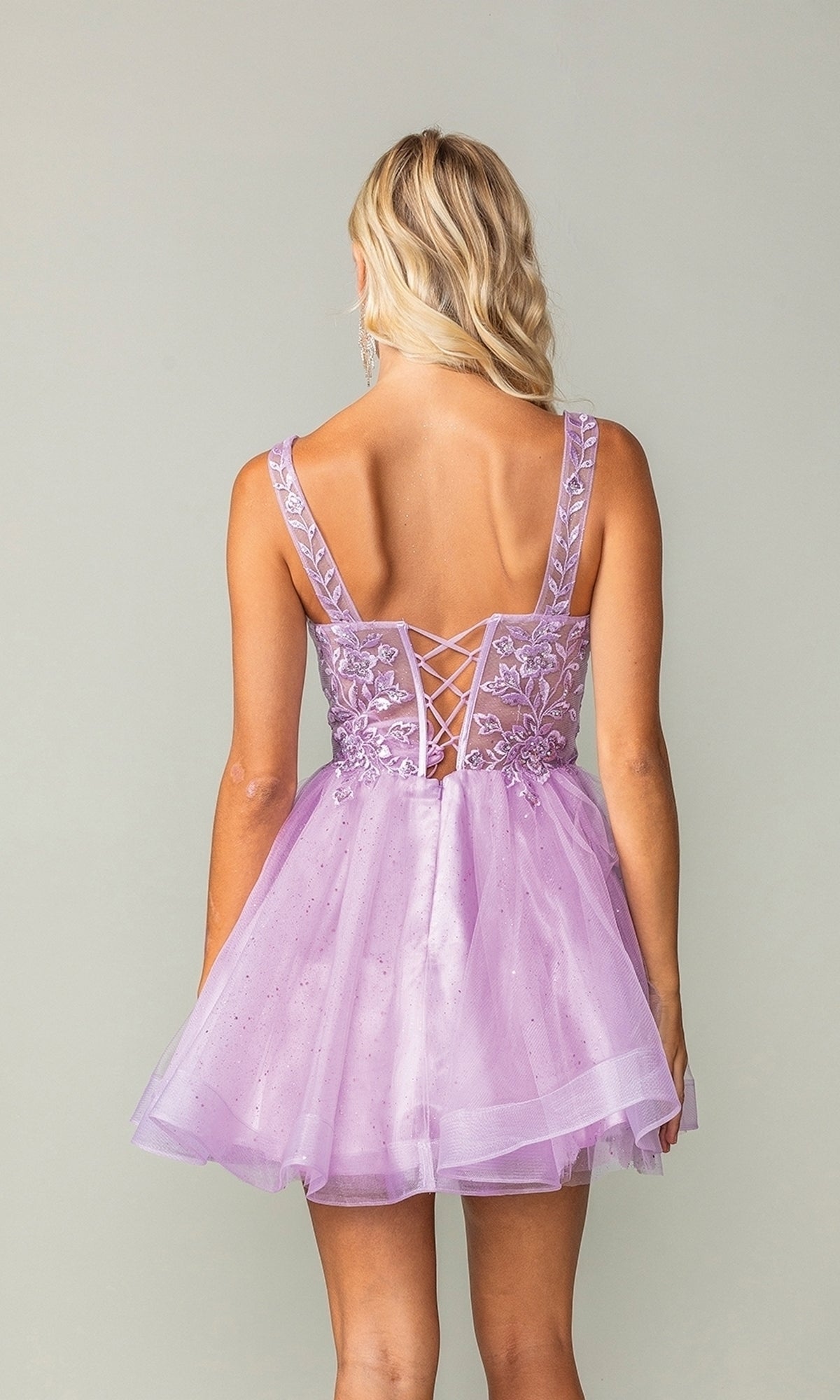 A blonde woman wears the Embroidered-Bodice Short Lace-Up Hoco Dress 3390 in lavender, with a lace-up back and floral embroidery, standing against a plain background.